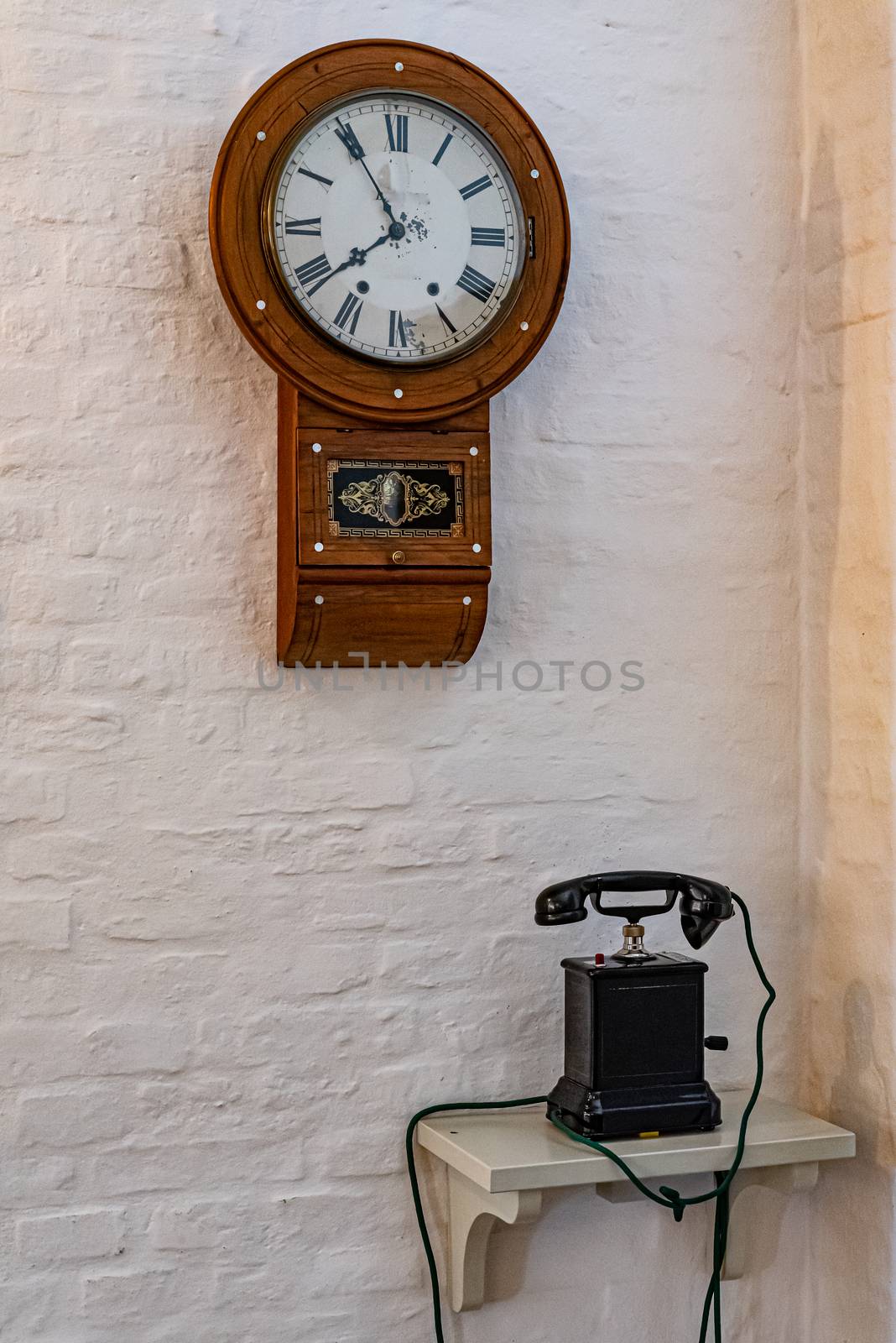 Antique wooden telephone and clock on white wall by brambillasimone