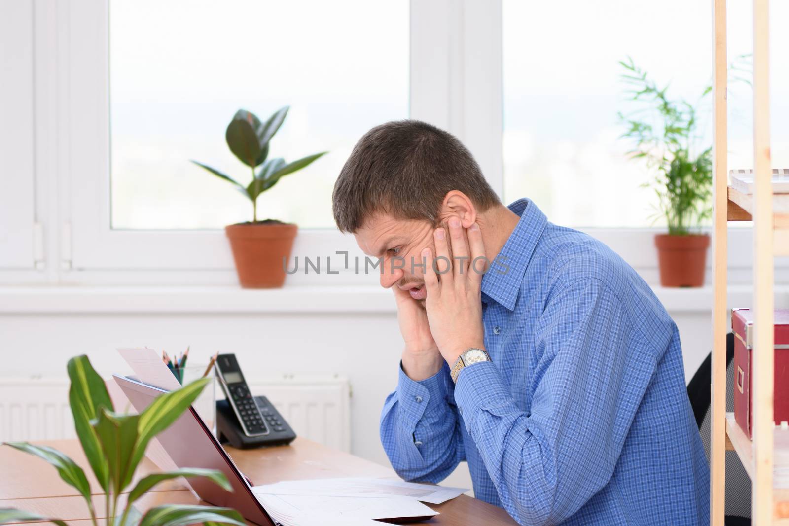 Office clerk grimacing grimacing pain on his face looking at a laptop