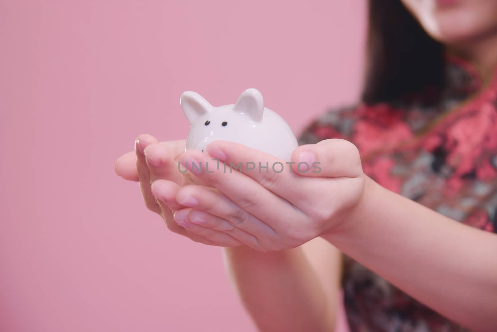 Little Piggy bank in young women hand on pink blackground, money savings concept.