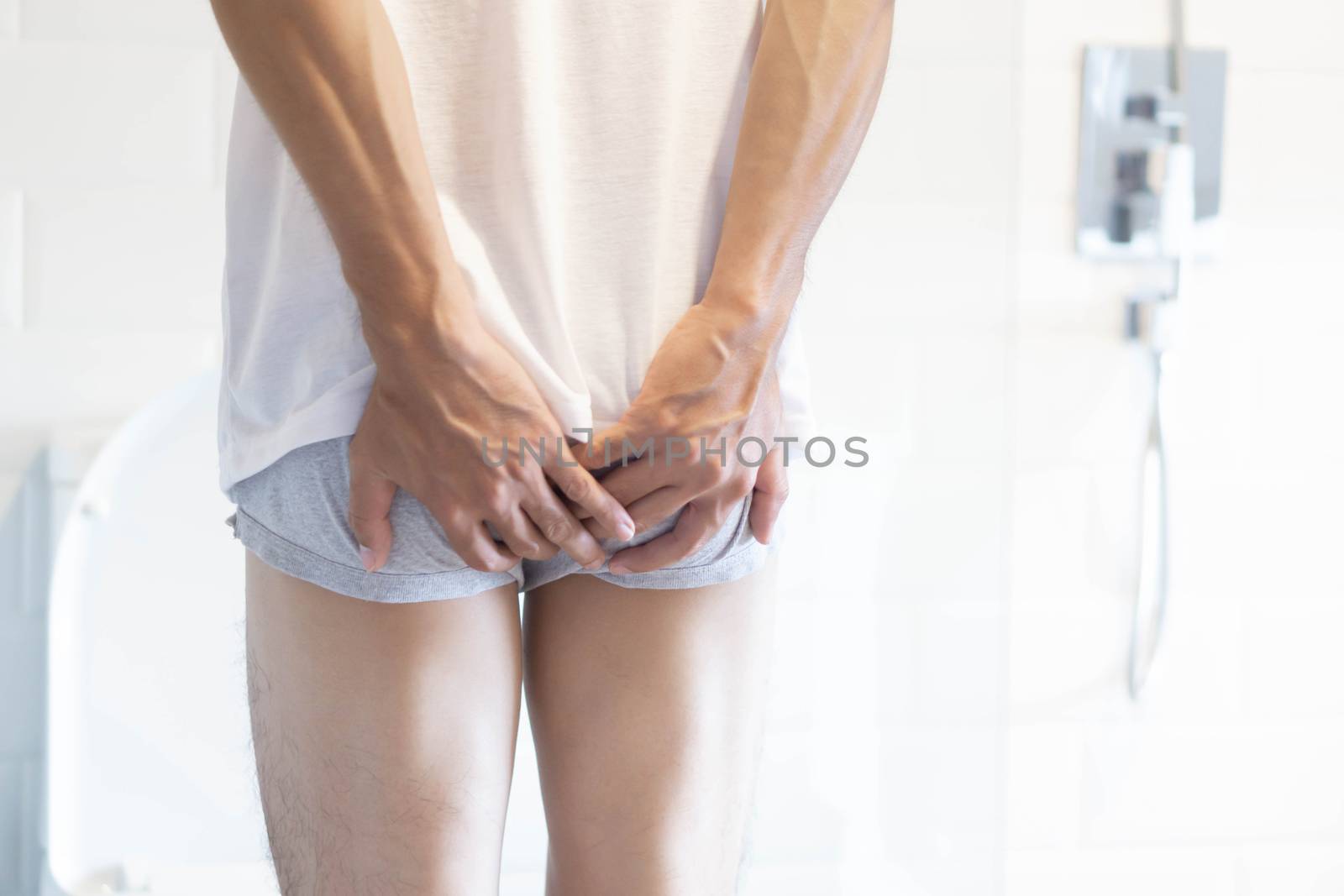 Closeup man holding bladder with pee pain in the toilet, selective focus