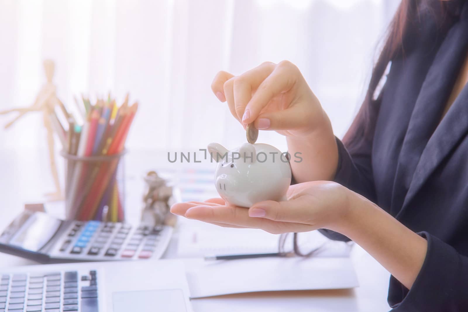 Coins on hand are dropped Piggy bank on wooden top table, money savings concept 
