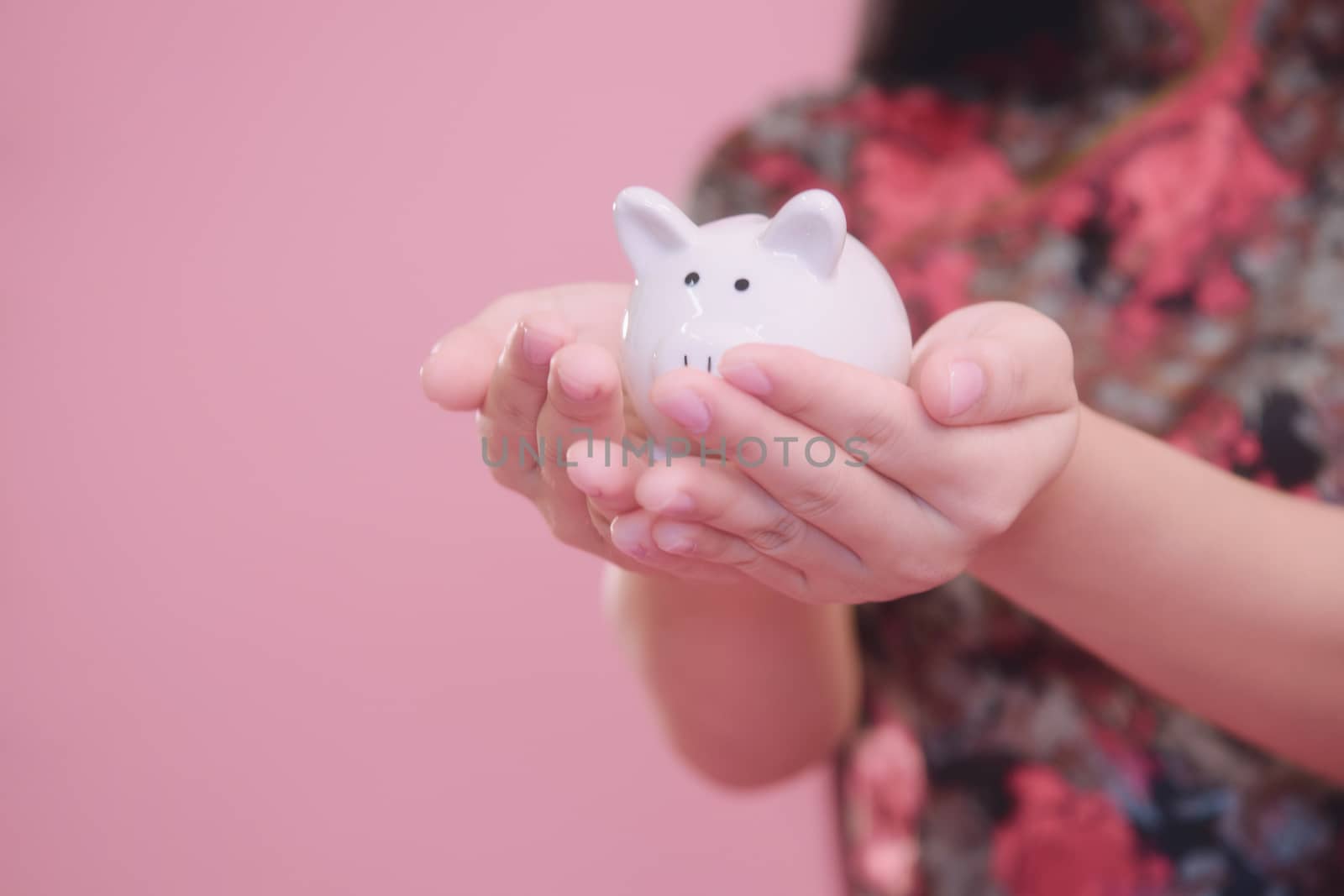 Little Piggy bank in young women hand on pink blackground, money savings concept.