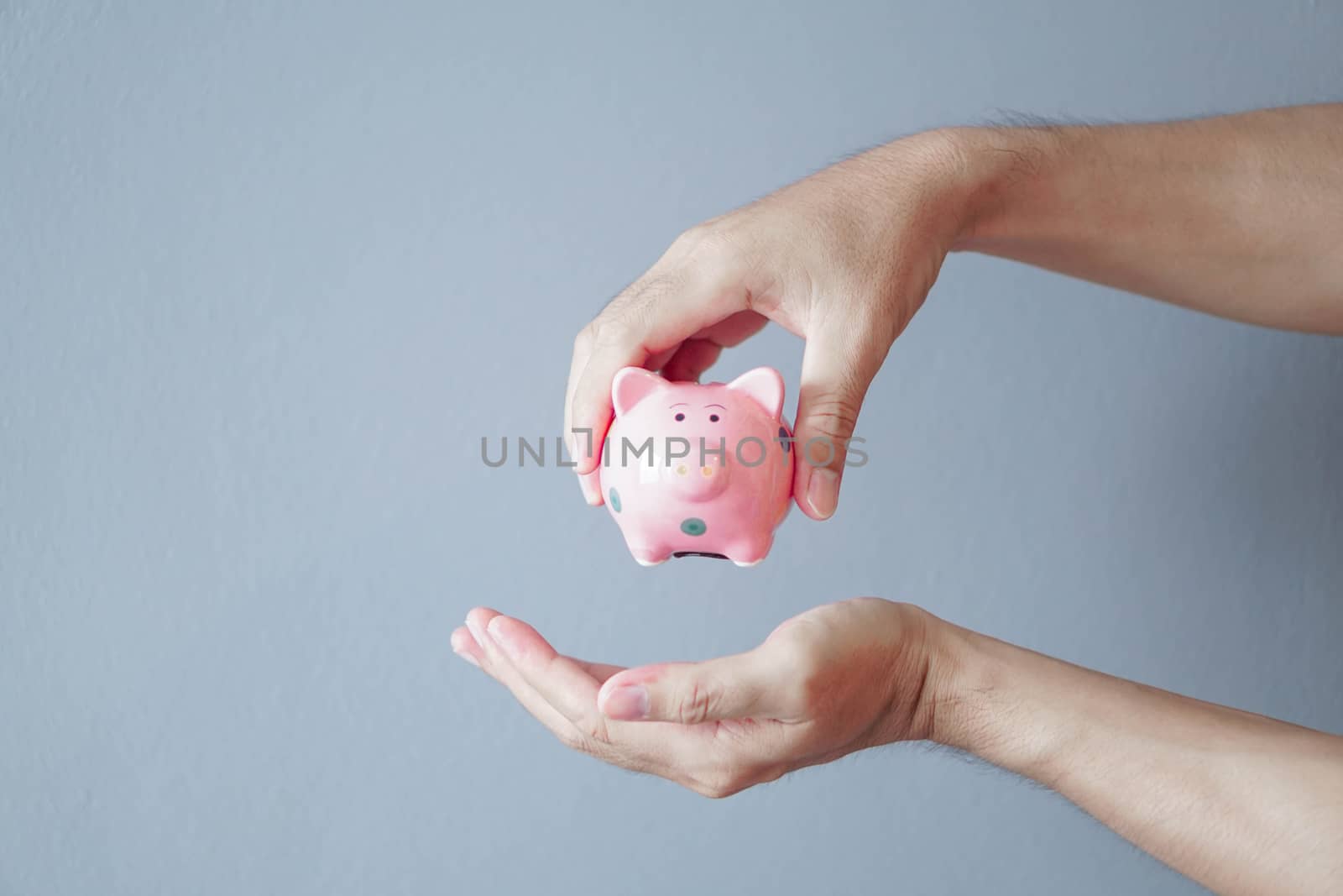 Closeup hand holding pink ceramic piggy bank on grey background, saving money concept