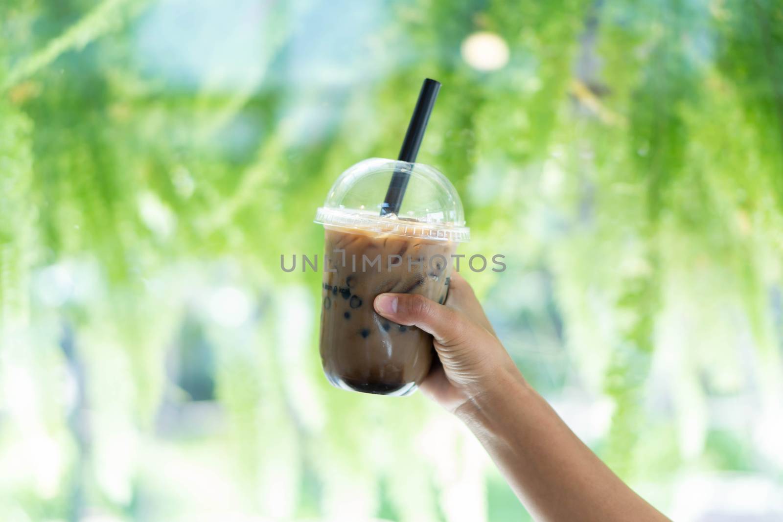 Closeup hand holding glass of ice coffee with bubble milk nature background