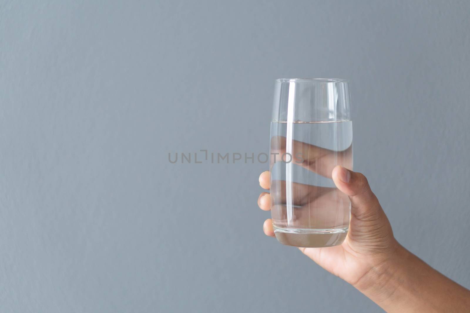 Close up woman hand holding a glass of pure water for dink with grey background, Health care concept