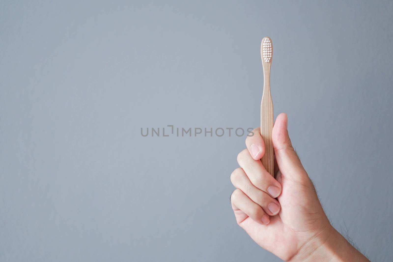Closeup man hand holding wooden toothbrush with grey background, health care concept
