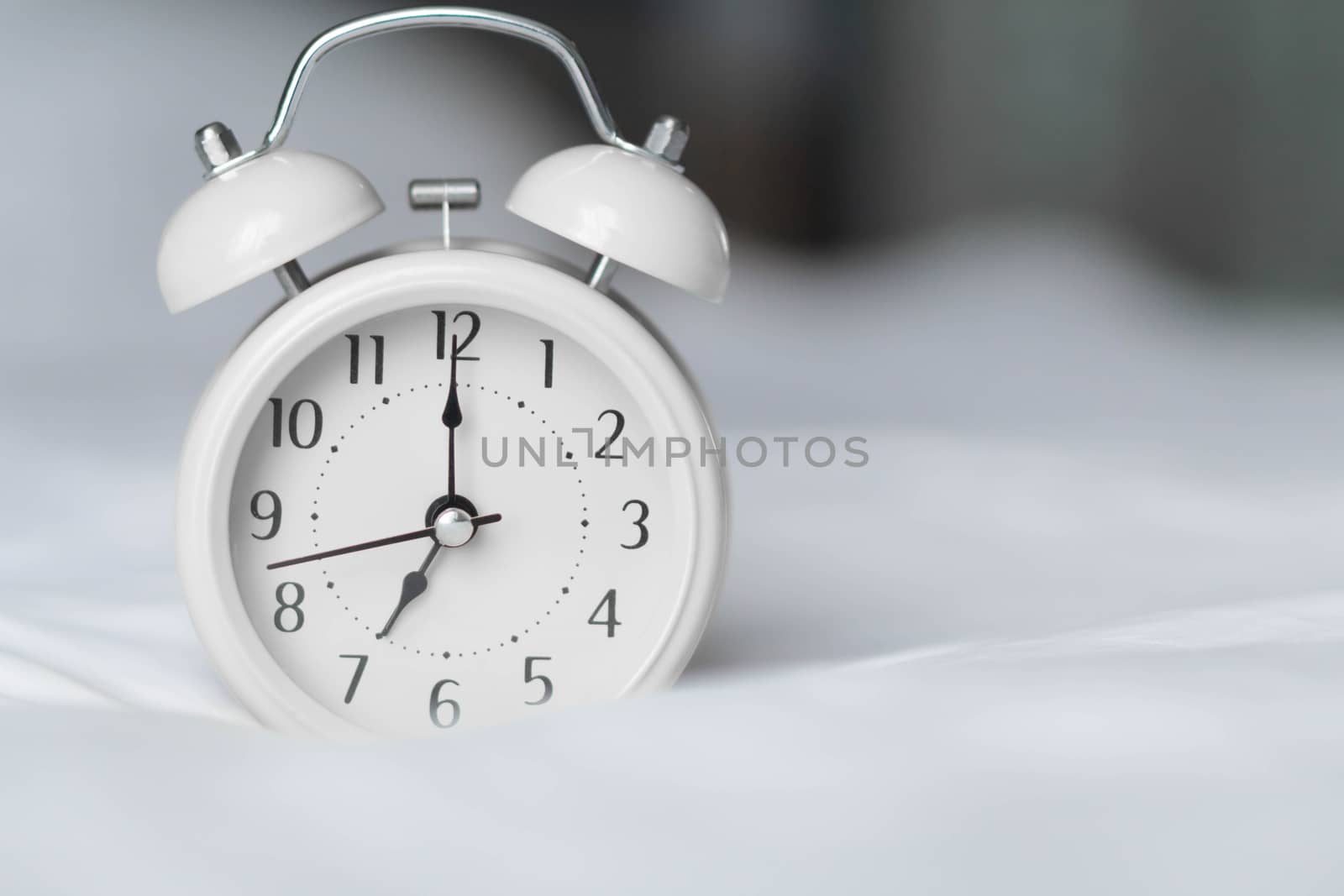 Alarm clock on white bad for wake up time with light from window, selective focus