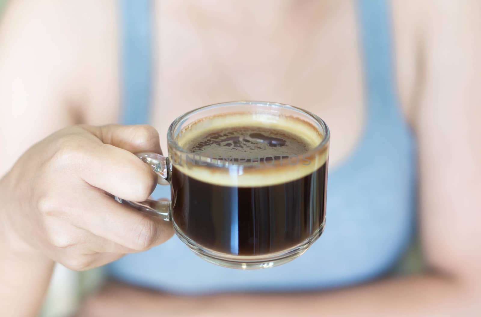 Closeup woman hand holding glass of hot americano coffee, selective focus, vintage tone