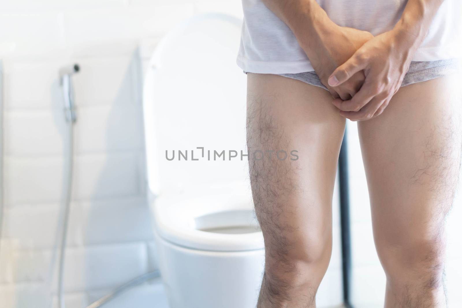 Closeup man holding bladder with pee pain in the toilet, selective focus