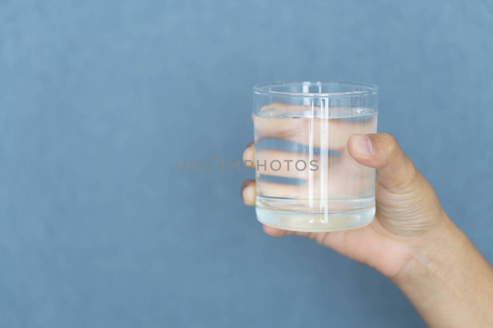 Close up woman hand holding a glass of pure water for dink with grey background, Health care concept