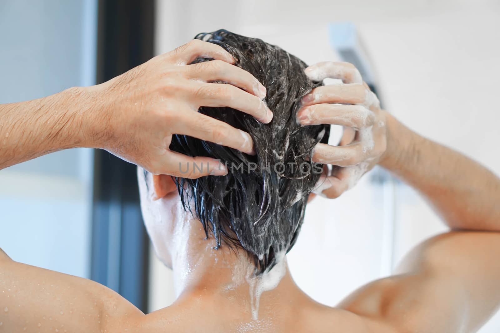 Closeup young man washing hair with with shampoo in the bathroom, vintage tone, selective focus