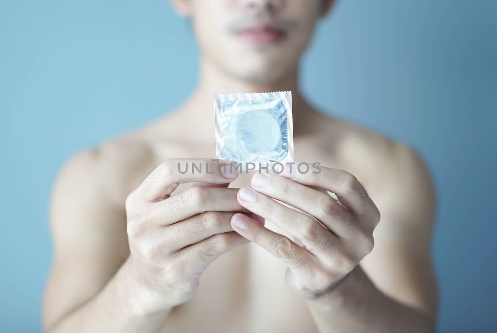 Close up man hand holding condom with blue background, health care and medical concept, selective focus