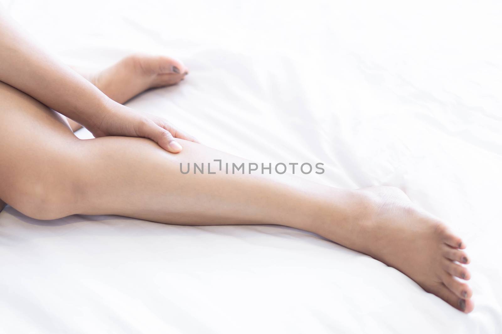 Close up woman touching her leg with pain lying on white bed, health care concept