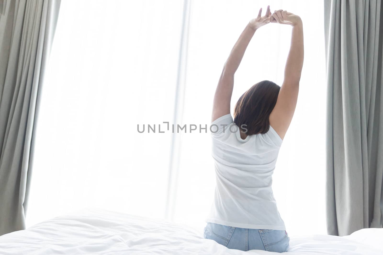 Close up woman sitting on the bed and stretching after waking up for relax in the morning with over light background