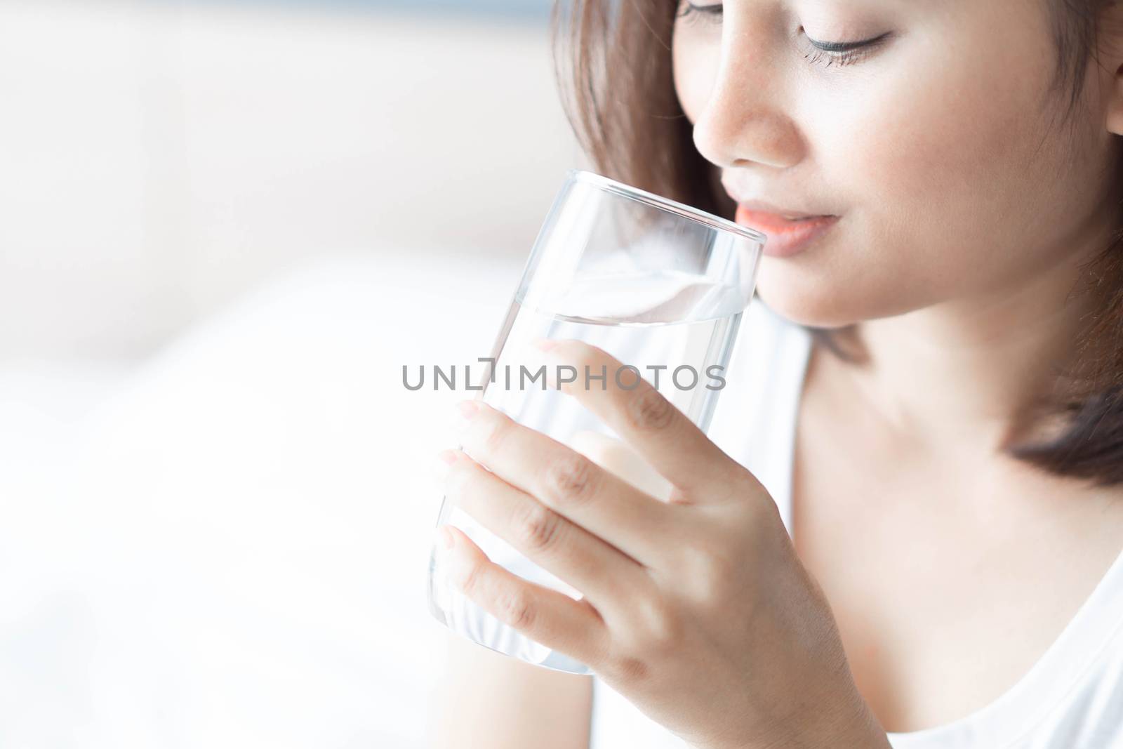 Close up woman drinking pure water from glass with light in the morning, Selective focus