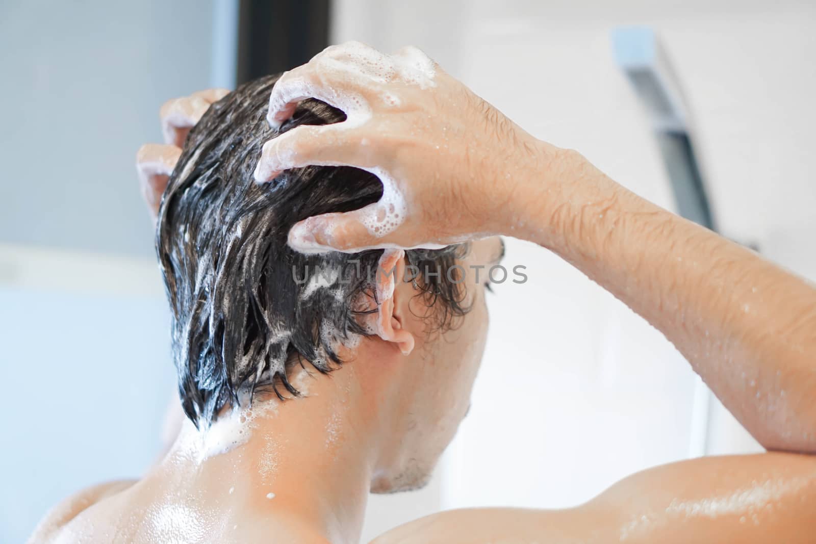 Closeup young man washing hair with with shampoo in the bathroom, vintage tone, selective focus