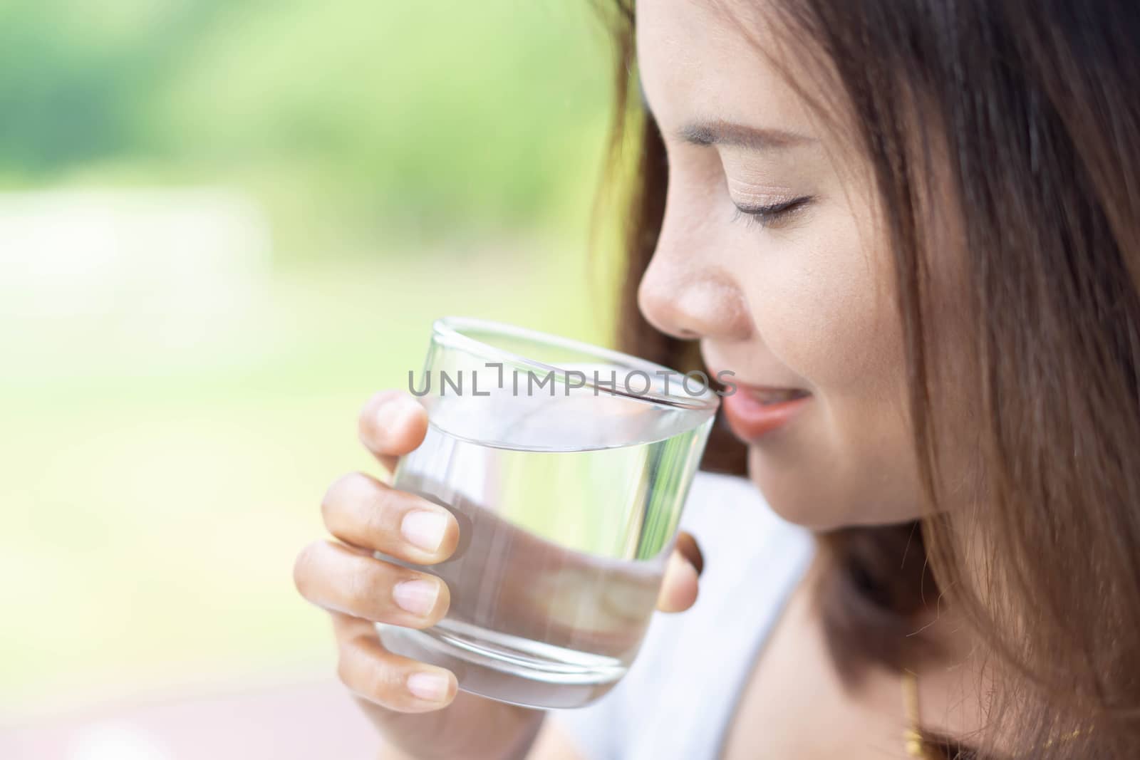 Close up woman drinking pure water from glass with light in the morning, Selective focus