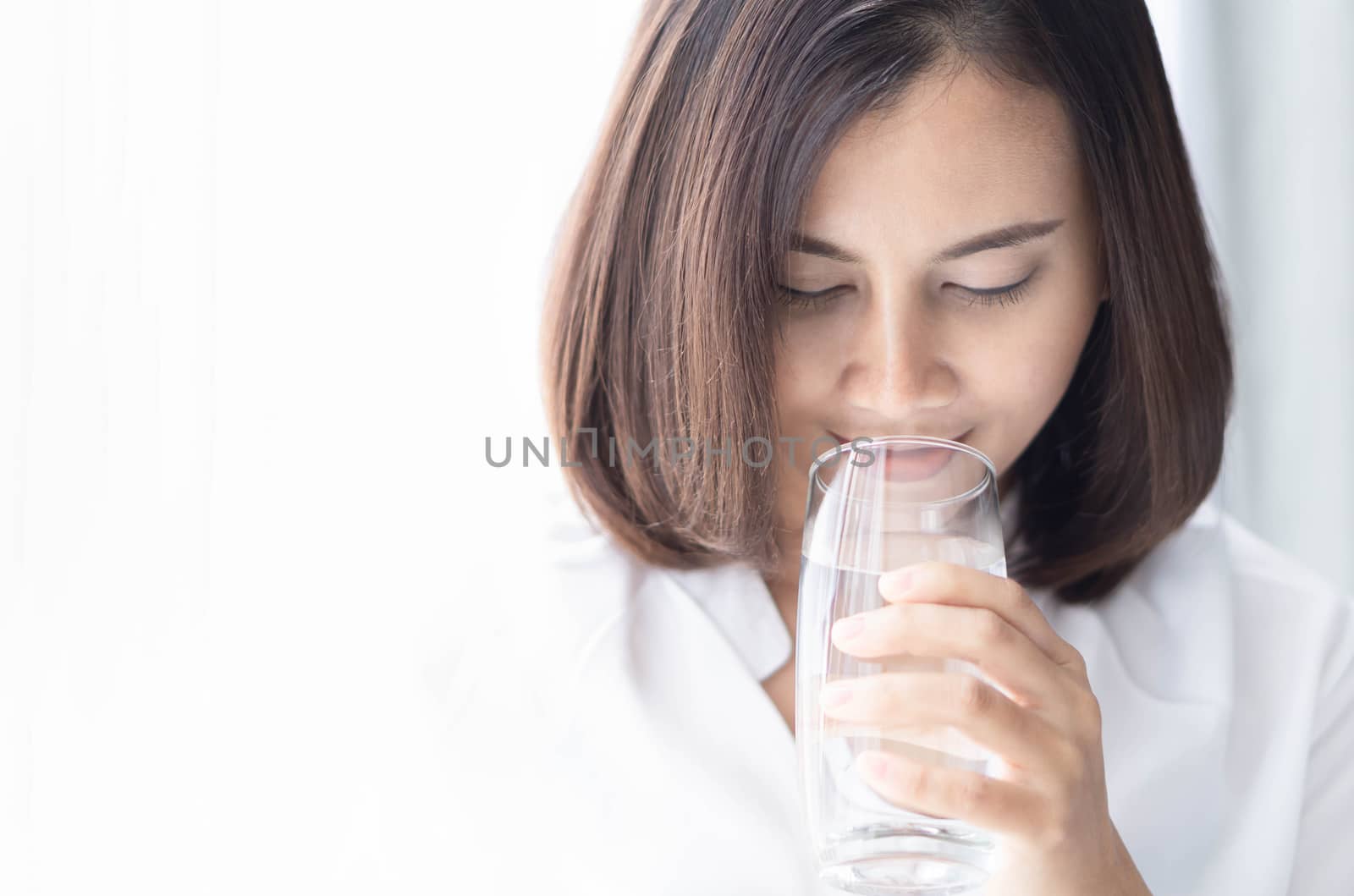 Close up woman drinking pure water from glass with light in the morning, Selective focus