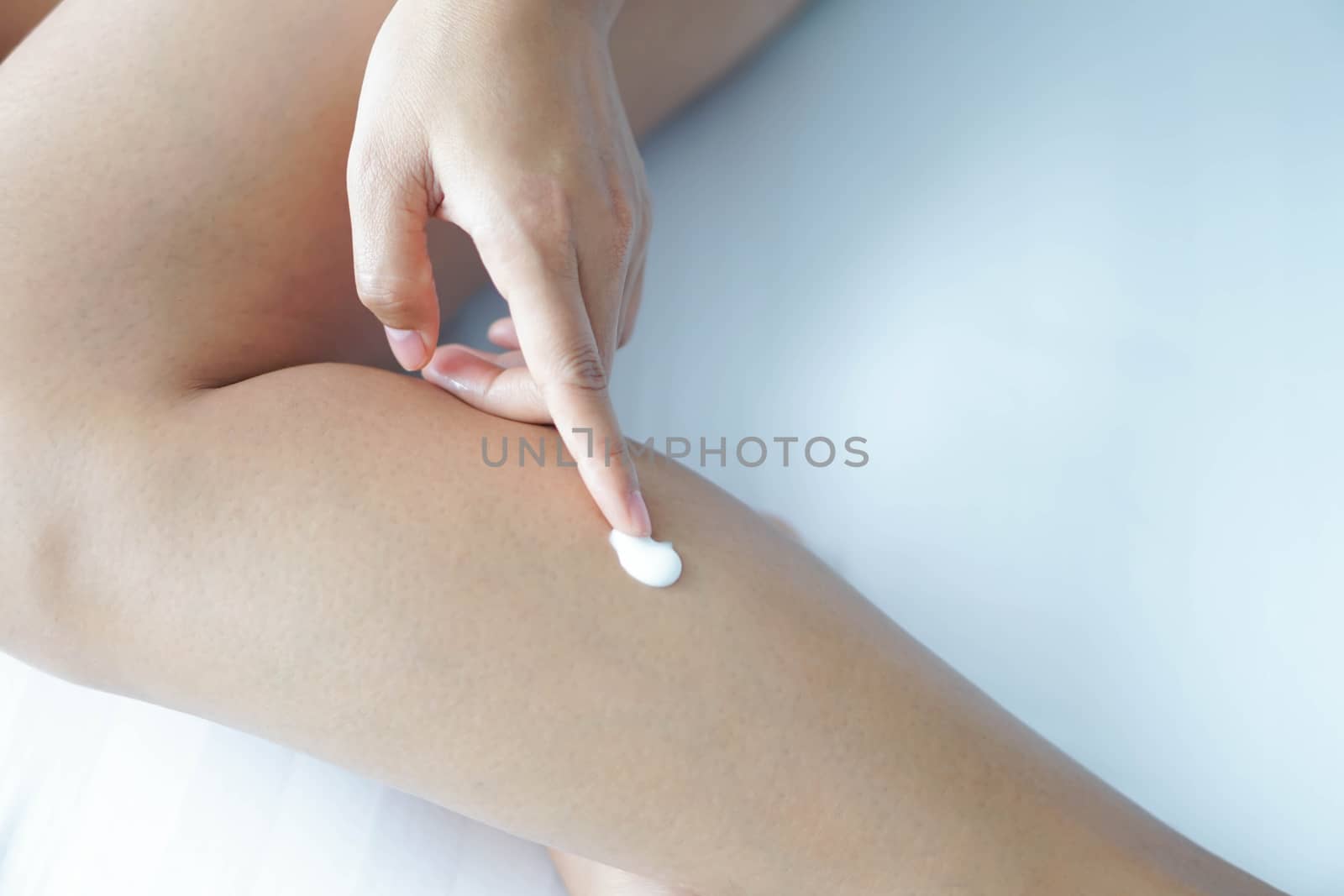 Woman hand applying cream or lotion on leg lying on white bed, selective focus