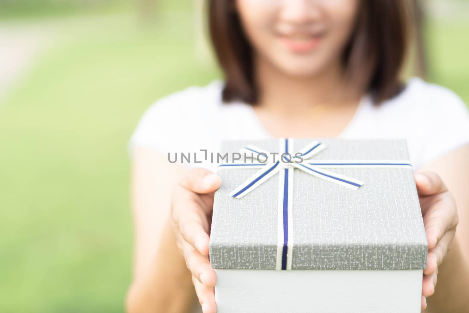 Woman hand holding grey gift box  on green nature background