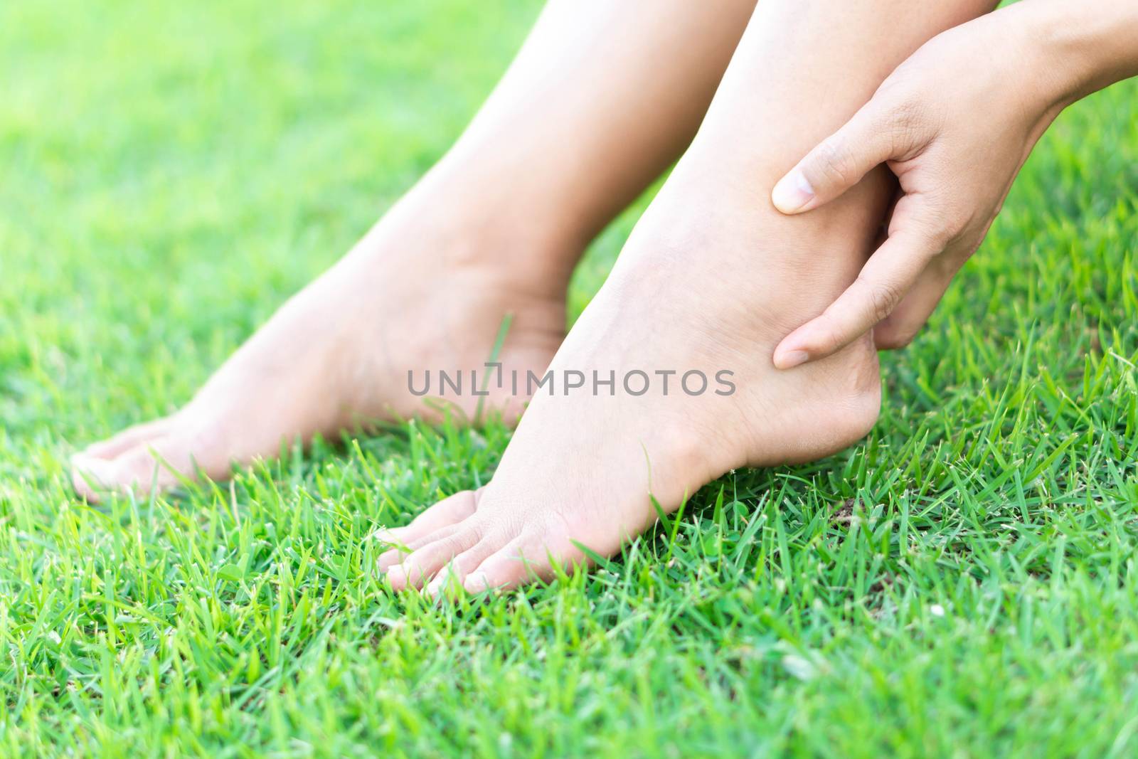 Woman hand holding foot with pain on green grass nature background, health care and medical concept