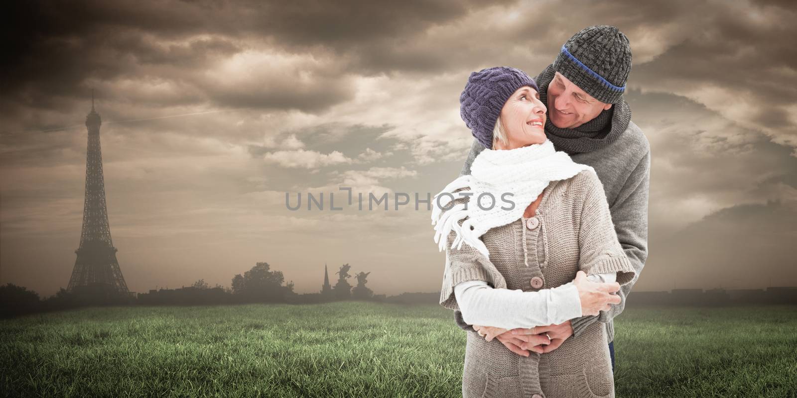 Happy mature couple in winter clothes embracing against paris under cloudy sky
