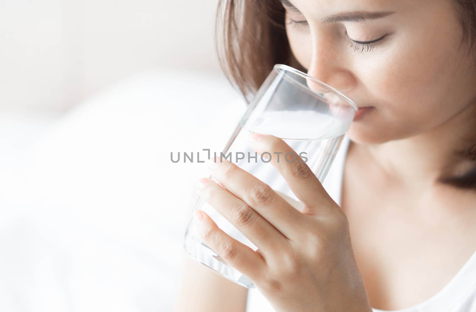 Close up woman drinking pure water from glass with light in the morning, Selective focus