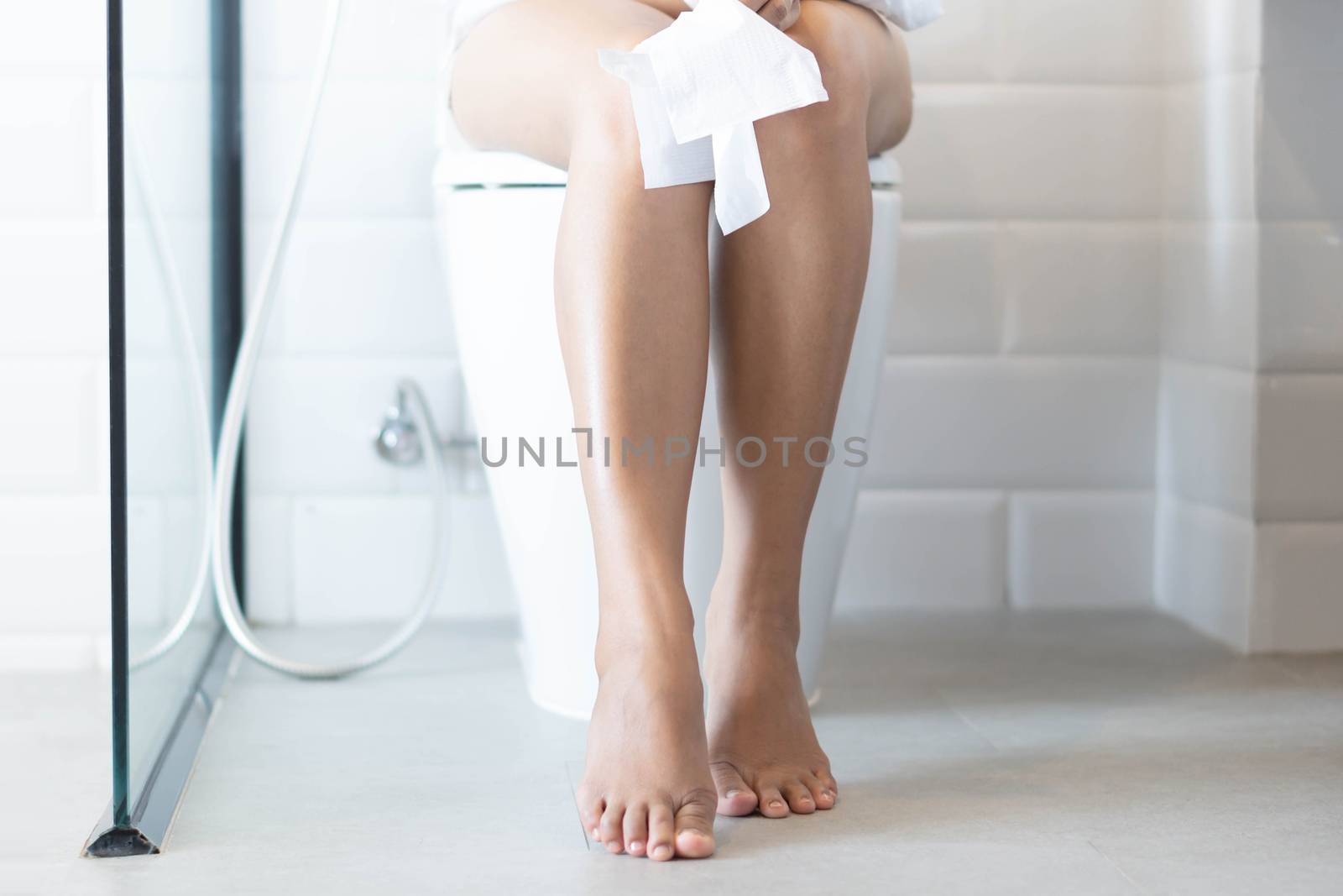 Closeup woman sitting on toilet with tissue paper in hand, selective focus