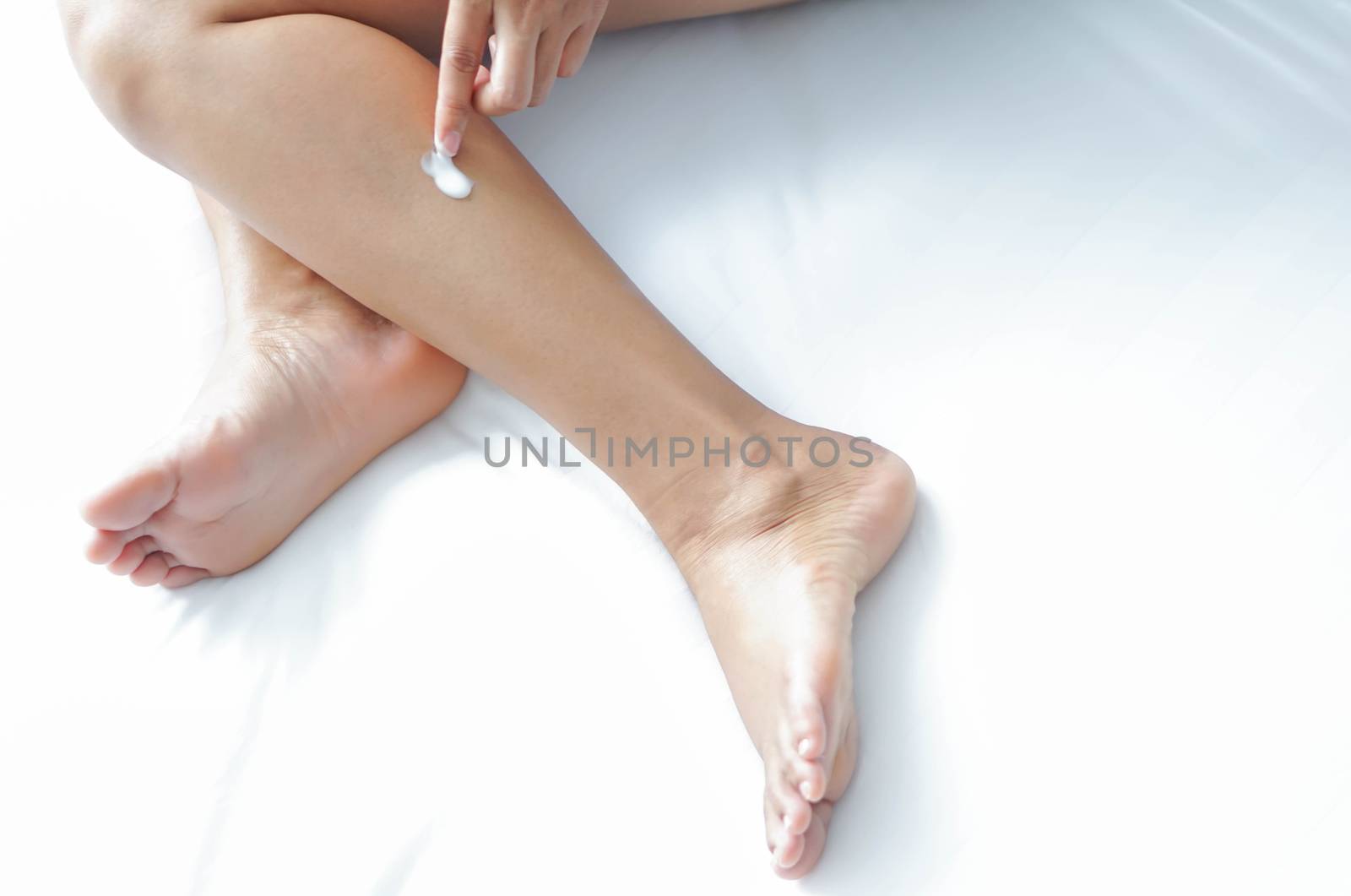 Woman hand applying cream or lotion on leg lying on white bed, selective focus