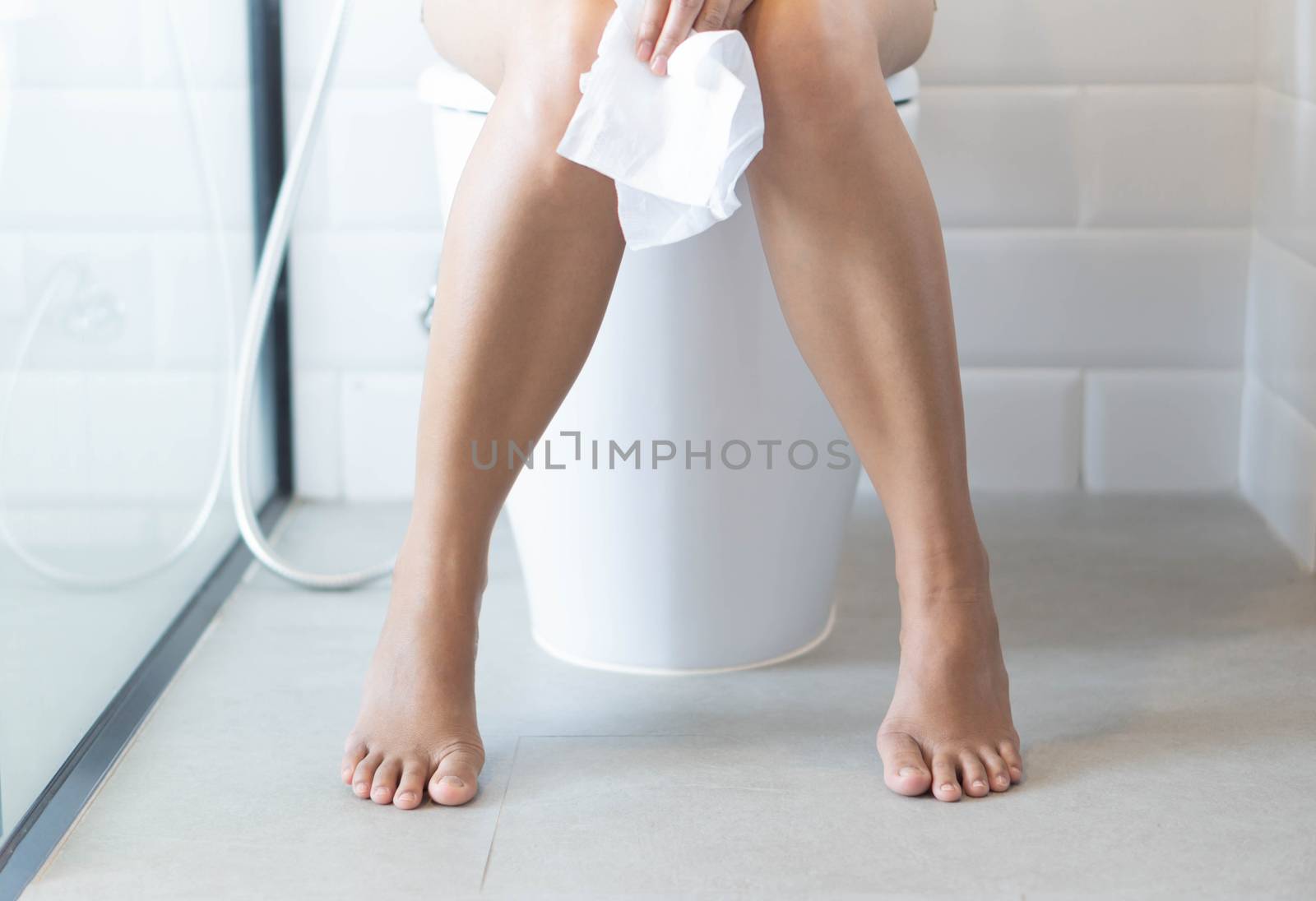 Closeup woman sitting on toilet with tissue paper in hand, selective focus