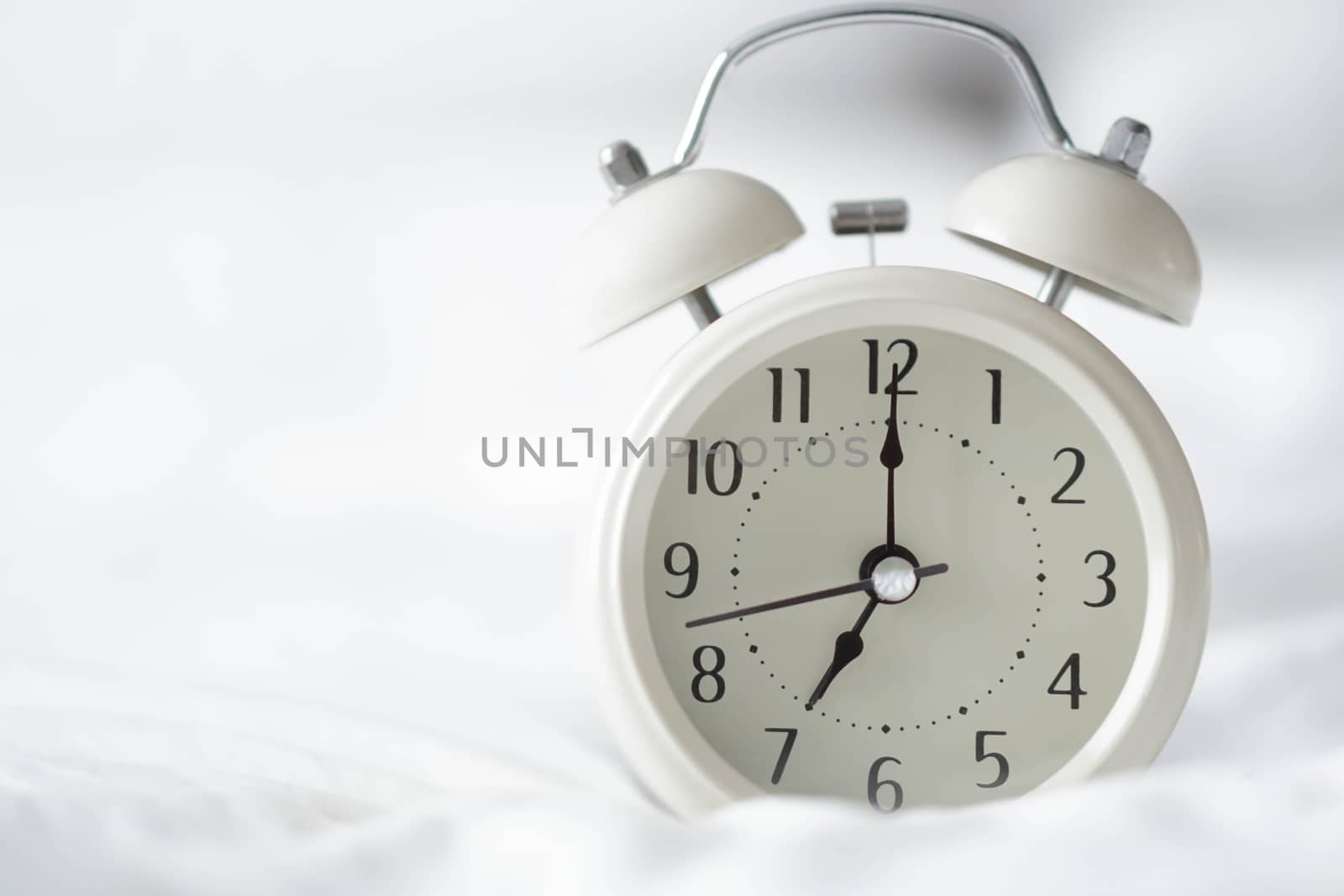 Alarm clock on white bad with light from window, selective focus