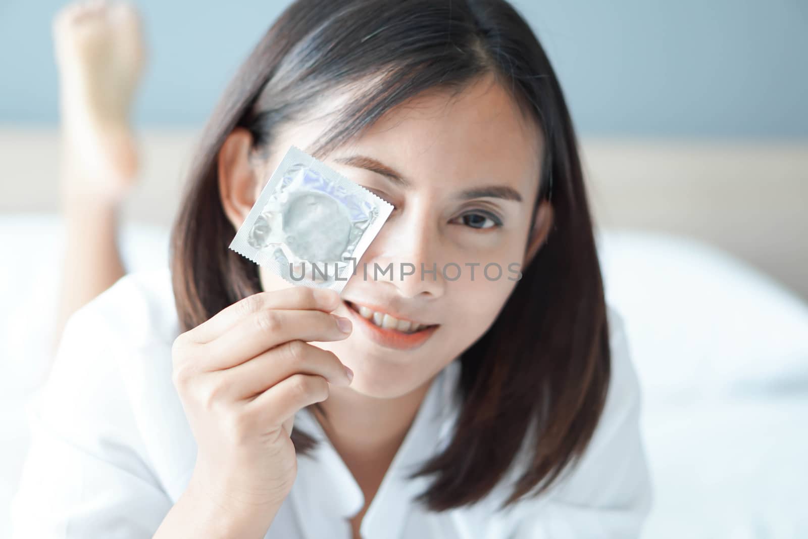 Close up woman hand holding condom with happy face lying on white bed, selective focus