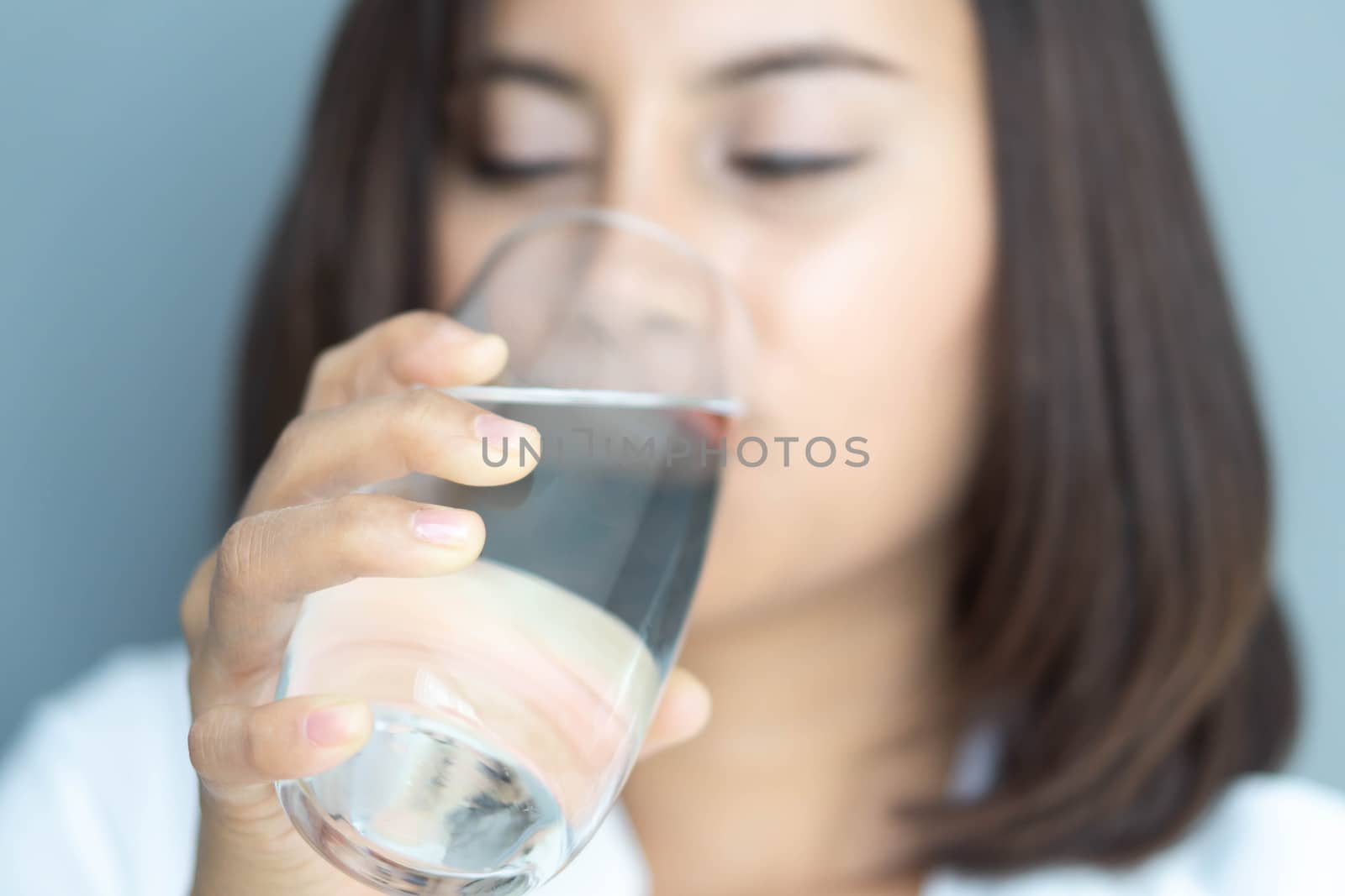 Close up woman drinking pure water from glass with blue background, Selective focus