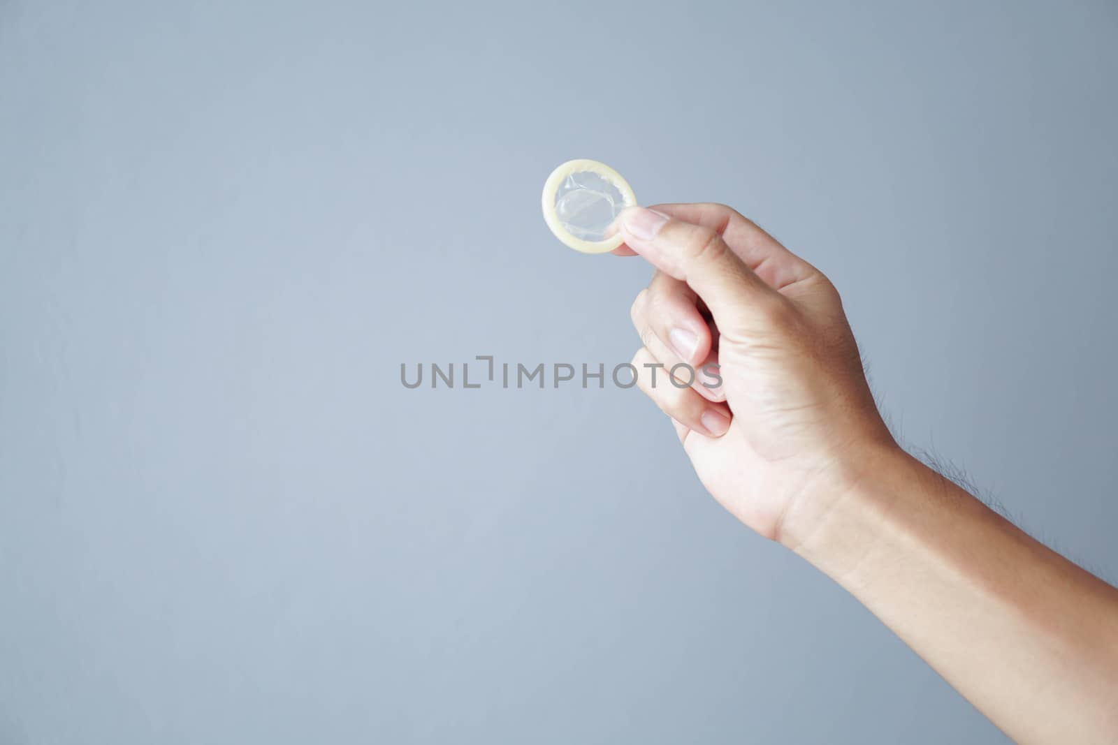 Close up man hand holding condom with grey background, health care and medical concept
