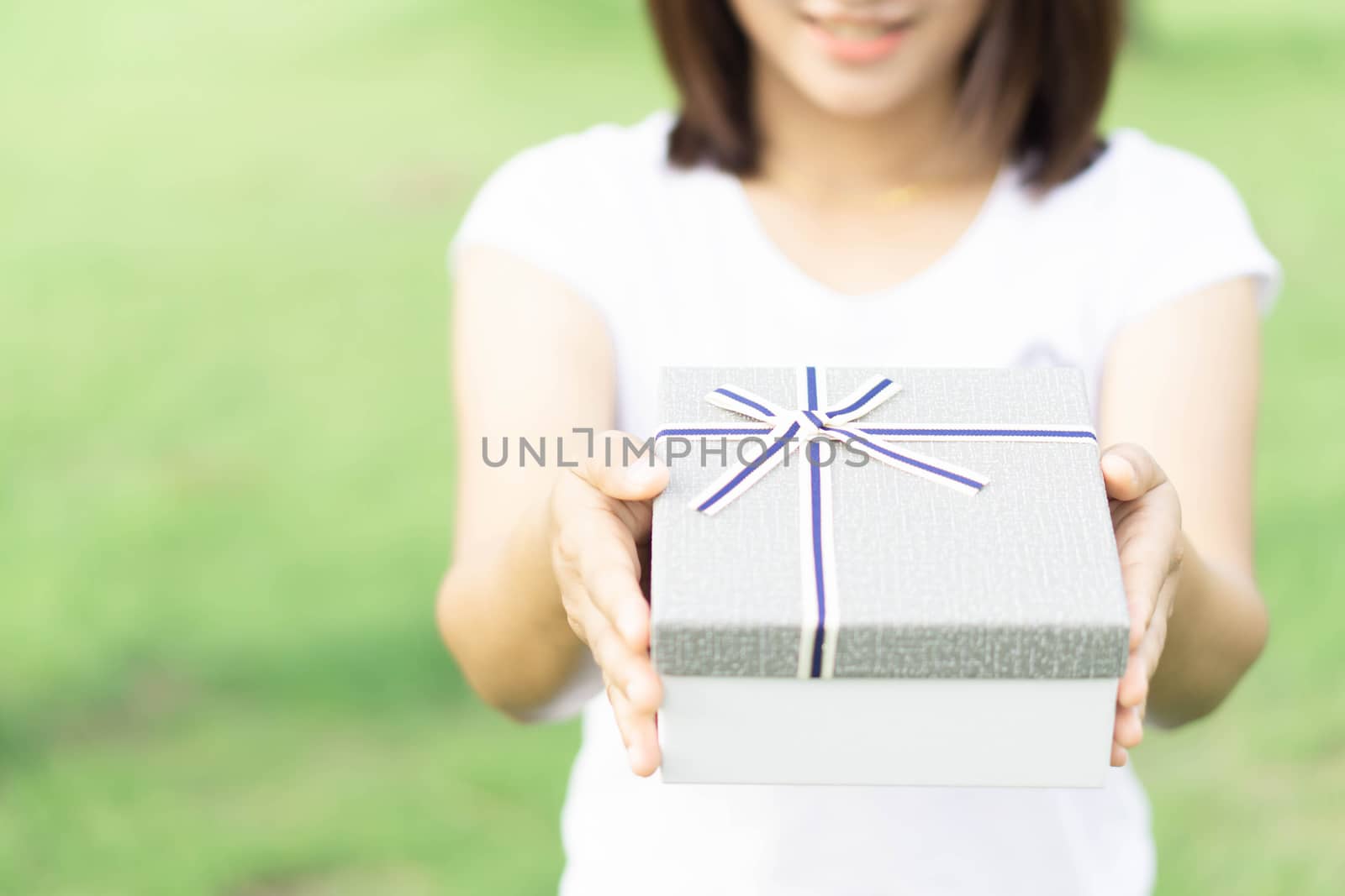 Woman hand holding grey gift box  on green nature background