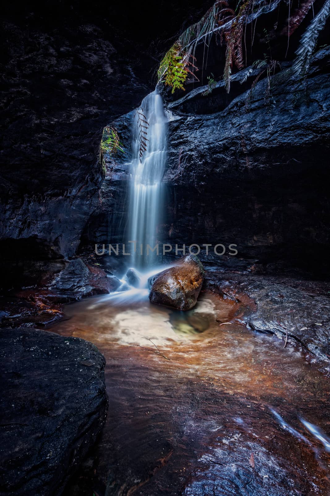 Waterfall tumbles over rock in a remote small dark canyon in Blue Mountains Australia