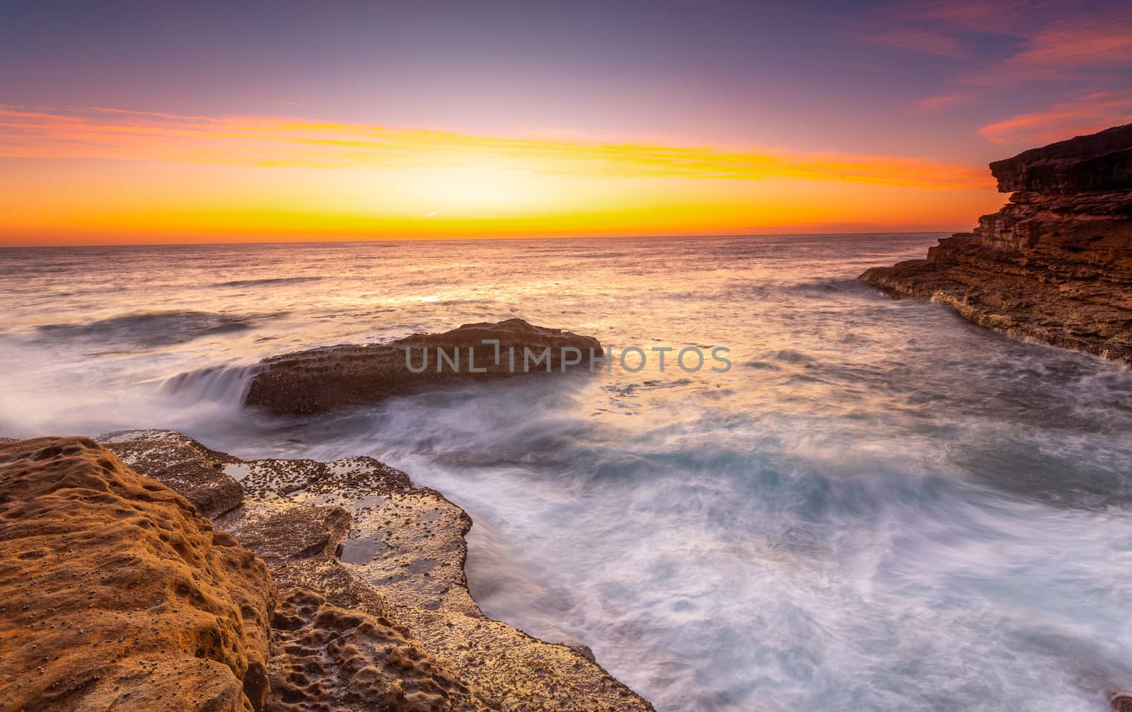 Sunrise over the ccean with some foreground rocks of eroded sand by lovleah