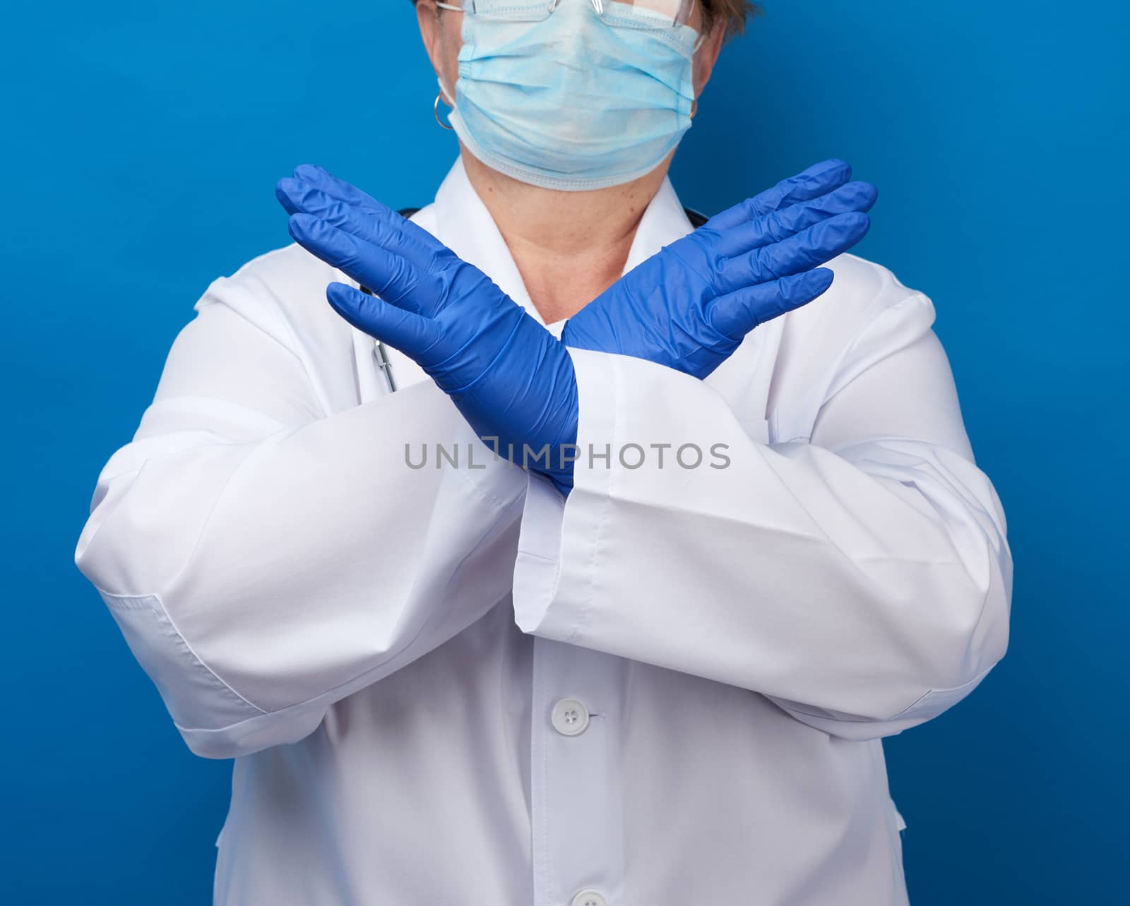female doctor dressed in a white medical gown and blue latex gloves, arms crossed in front of the chest, denial concept, stop