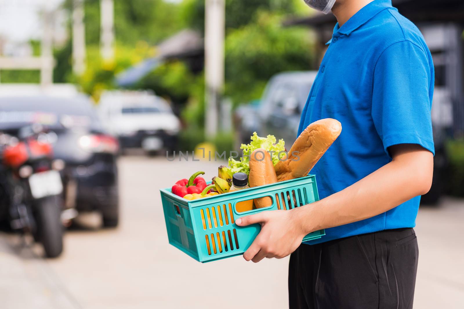 Asian grocery store delivery man wearing blue uniform and face mask protect he delivering fresh food vegetable in plastic box at door front home after coronavirus outbreak, back to new normal concept