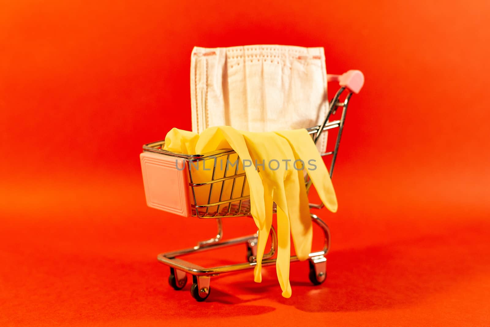 Shopping basket with a protective medical mask against coronavirus and latex gloves. Red background. by Pirlik