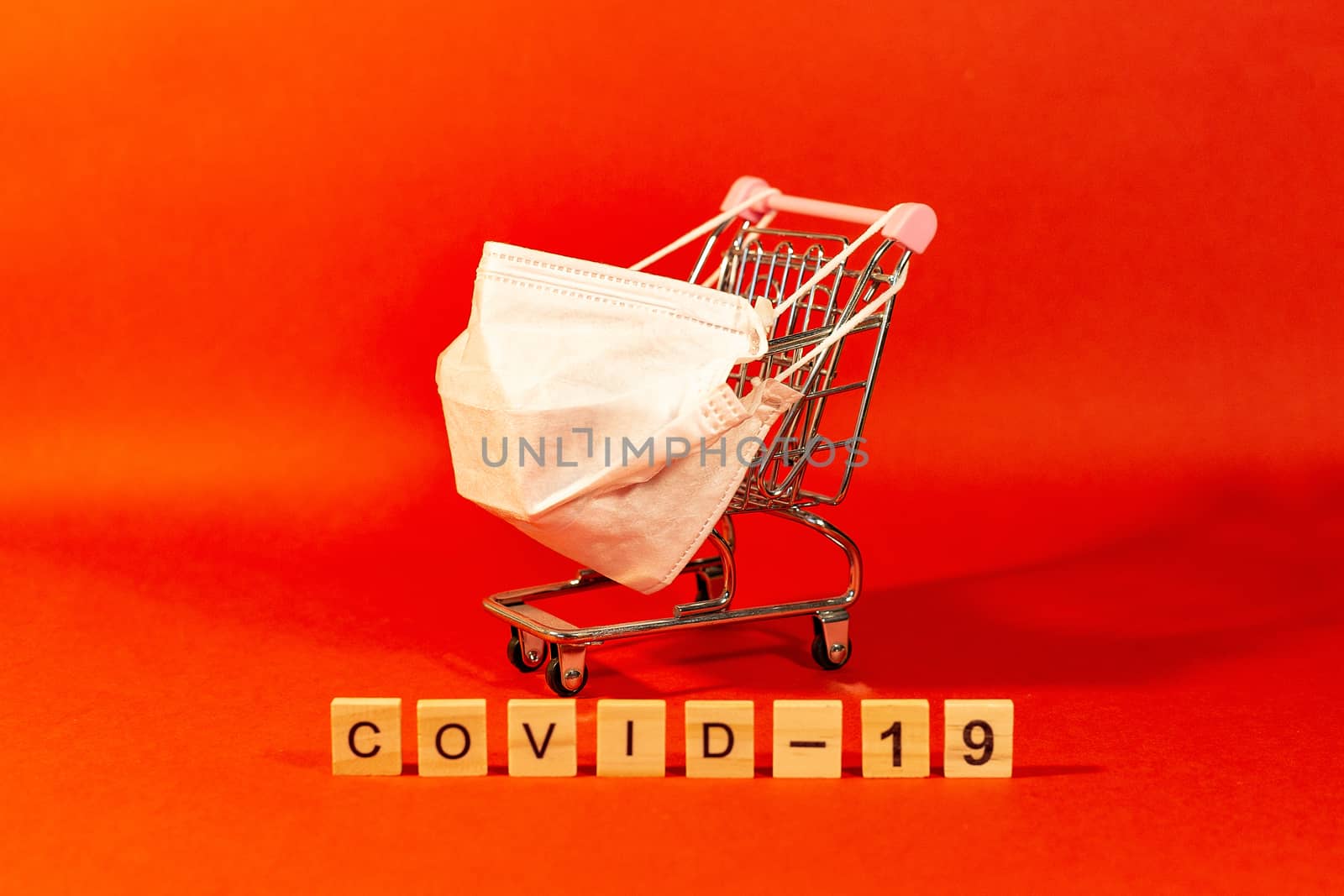 Shopping basket with a protective medical mask against coronavirus and latex gloves. Safe and online shopping . Red background. by Pirlik