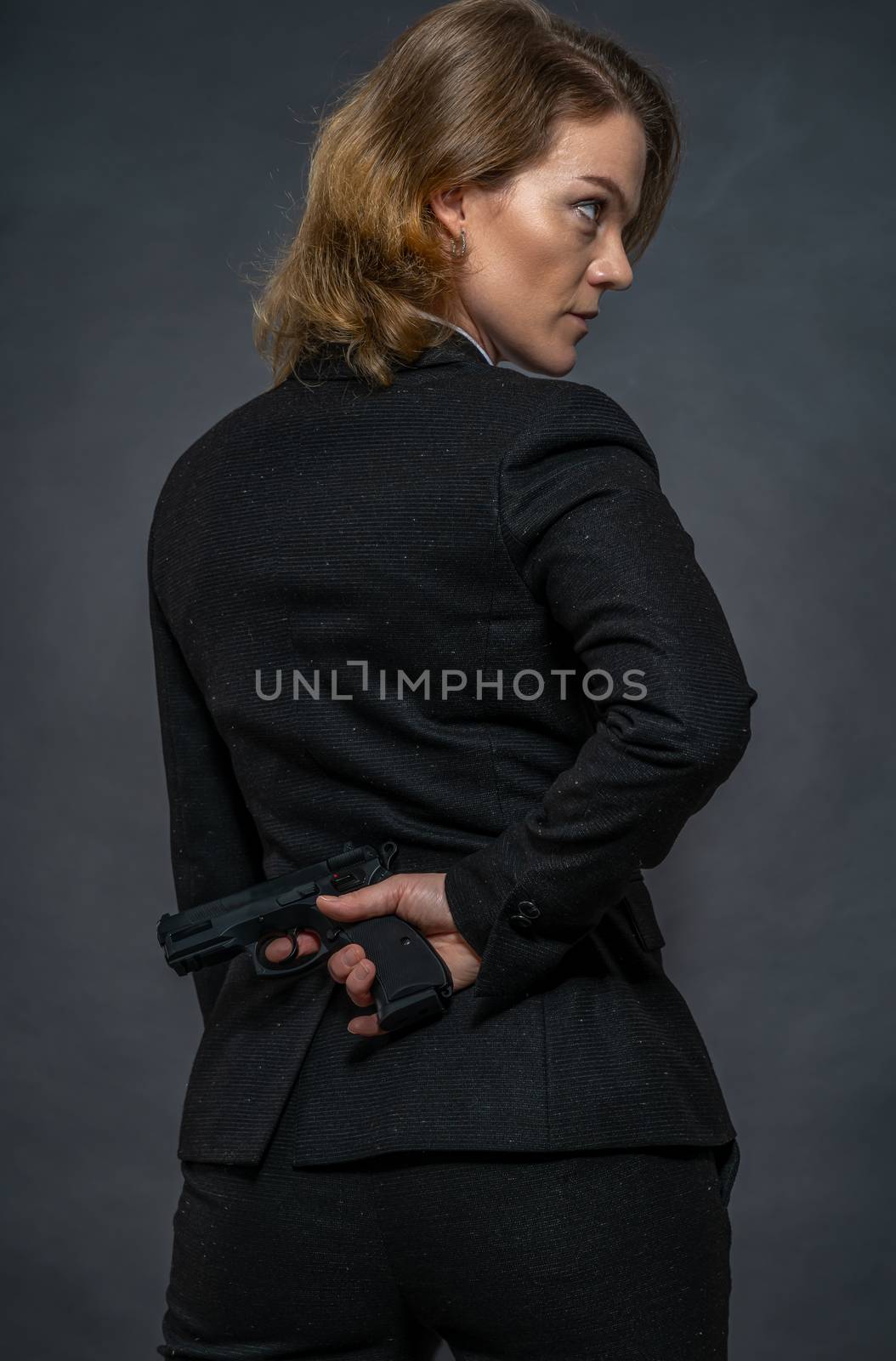 gun in hand behind the back of a woman in a suit.