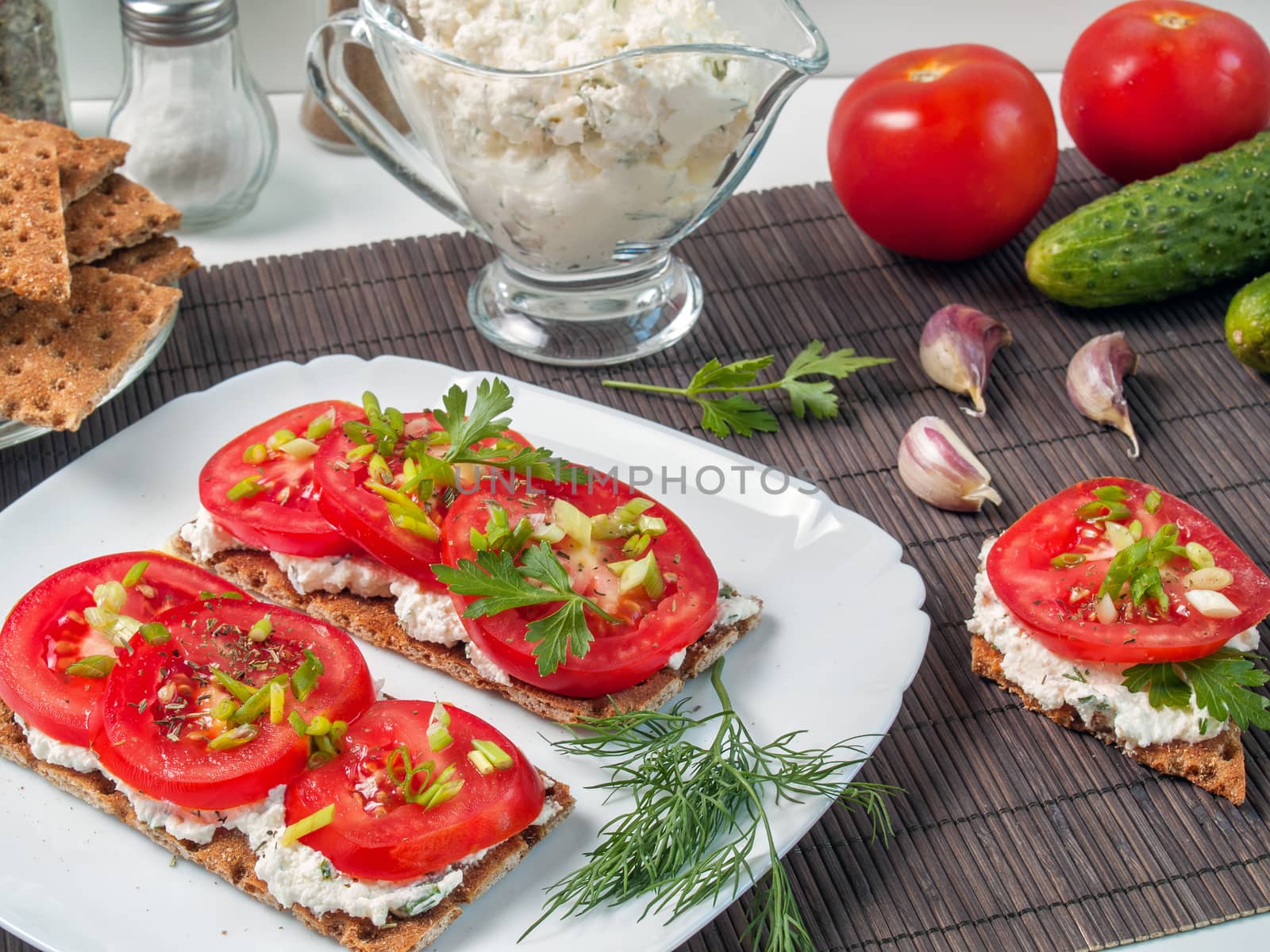Crispy bread from buckwheat flour smeared with curd cheese on top a tomato with greens and spices is shown close up