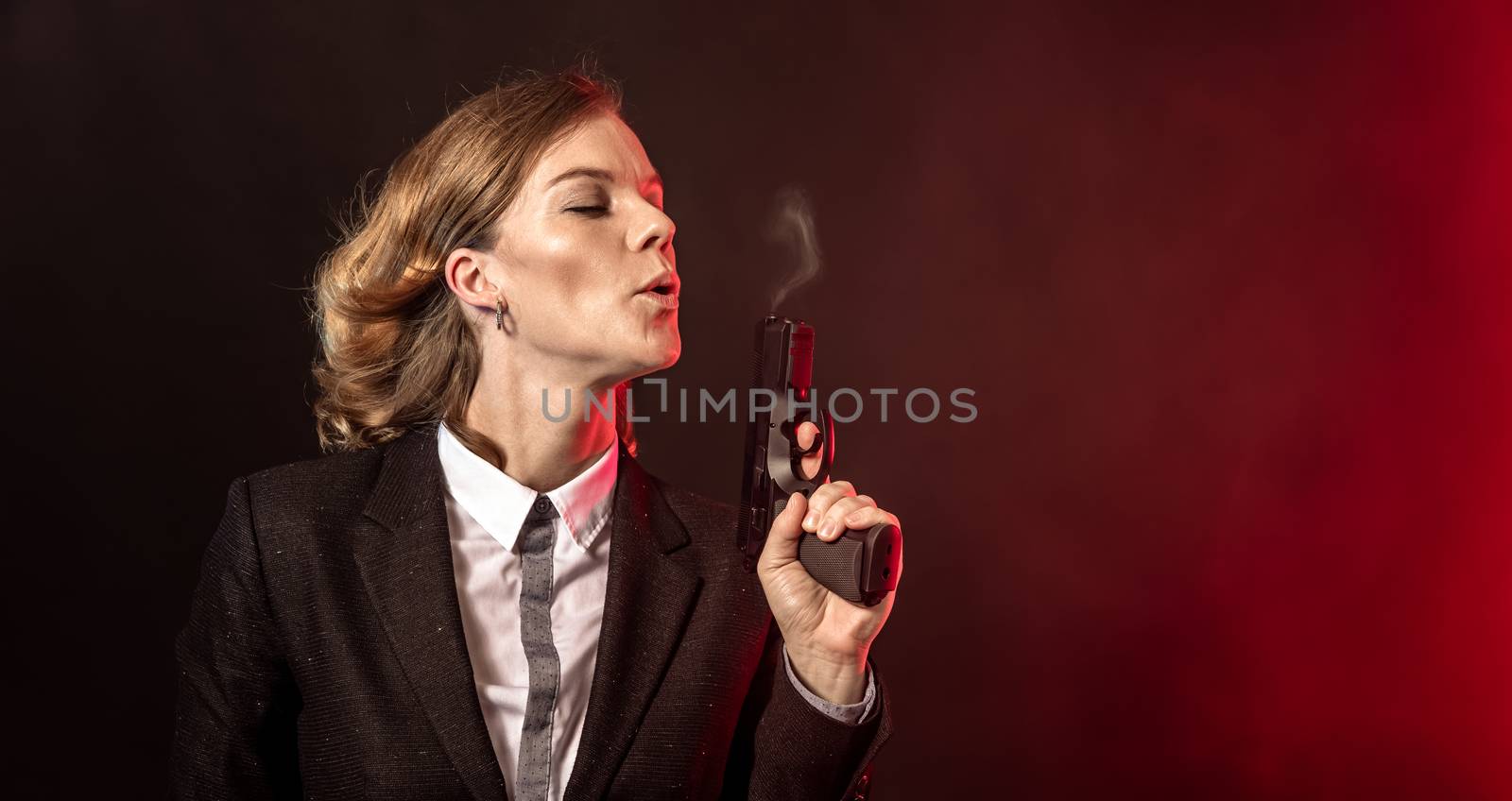 blowing smoke out of a gun after a shot. portret of a business woman on a dark background. banner with copy space.