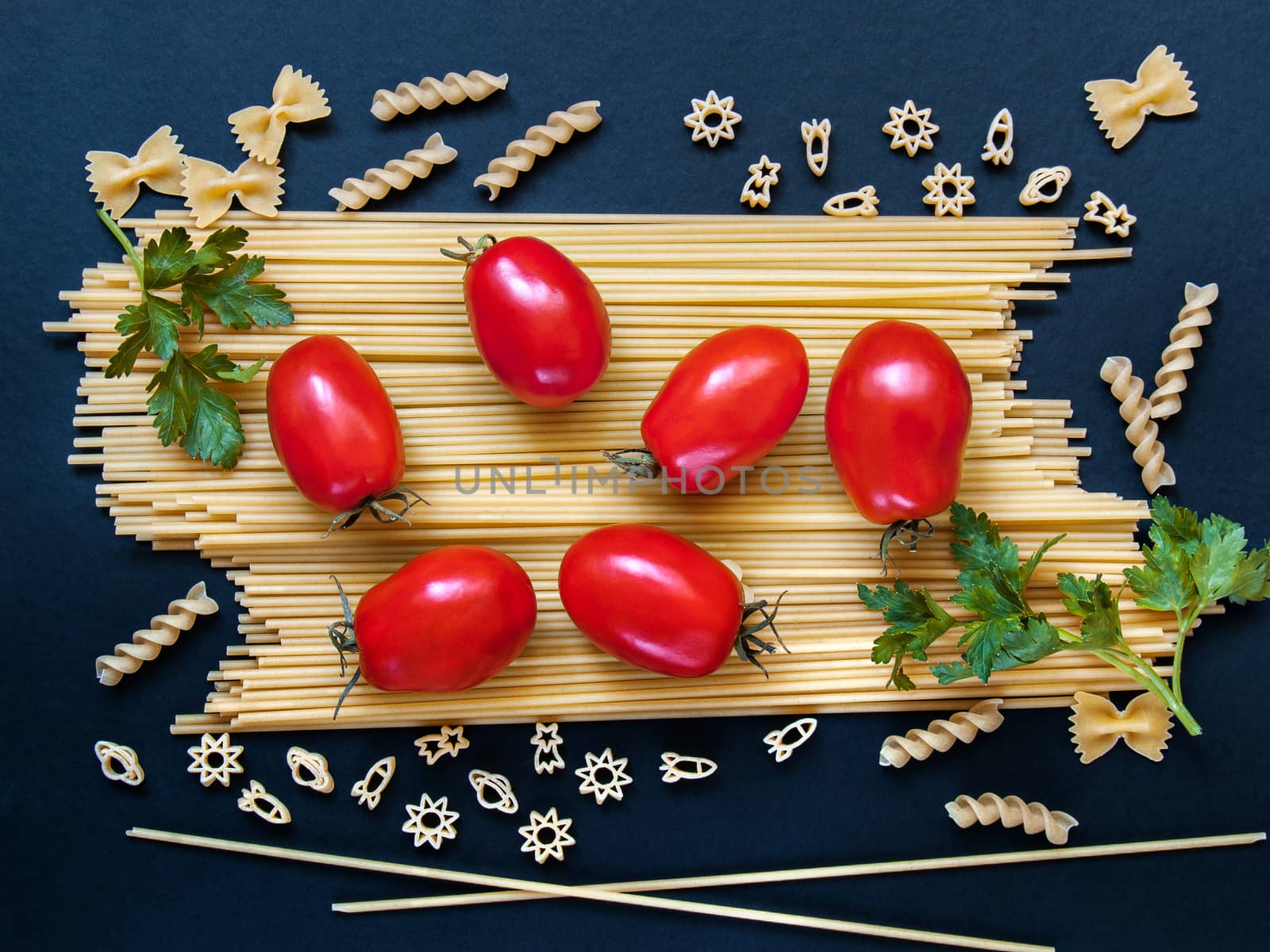 Spaghetti with tomatoes, greens and other figured pasta in the form of bows, spirals, figures of rockets and stars for cooking on a dark background