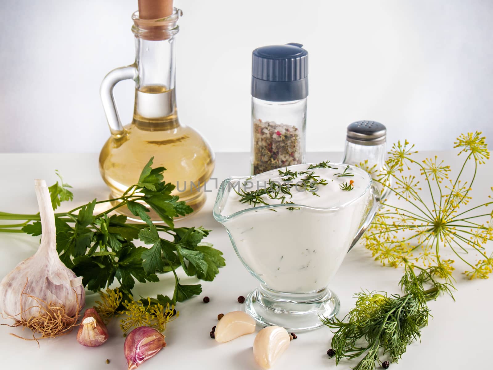 Cooked sour cream sauce with garlic, herbs, parsley, dill, herbs, pepper in a glass bowl on a white background with butter in a bottle, with pepper and salt jars