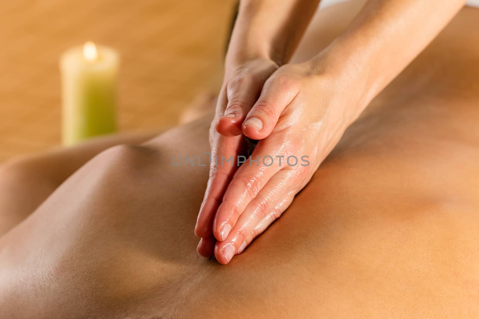 Close up detail of hands massaging female spinal column at candlelight.