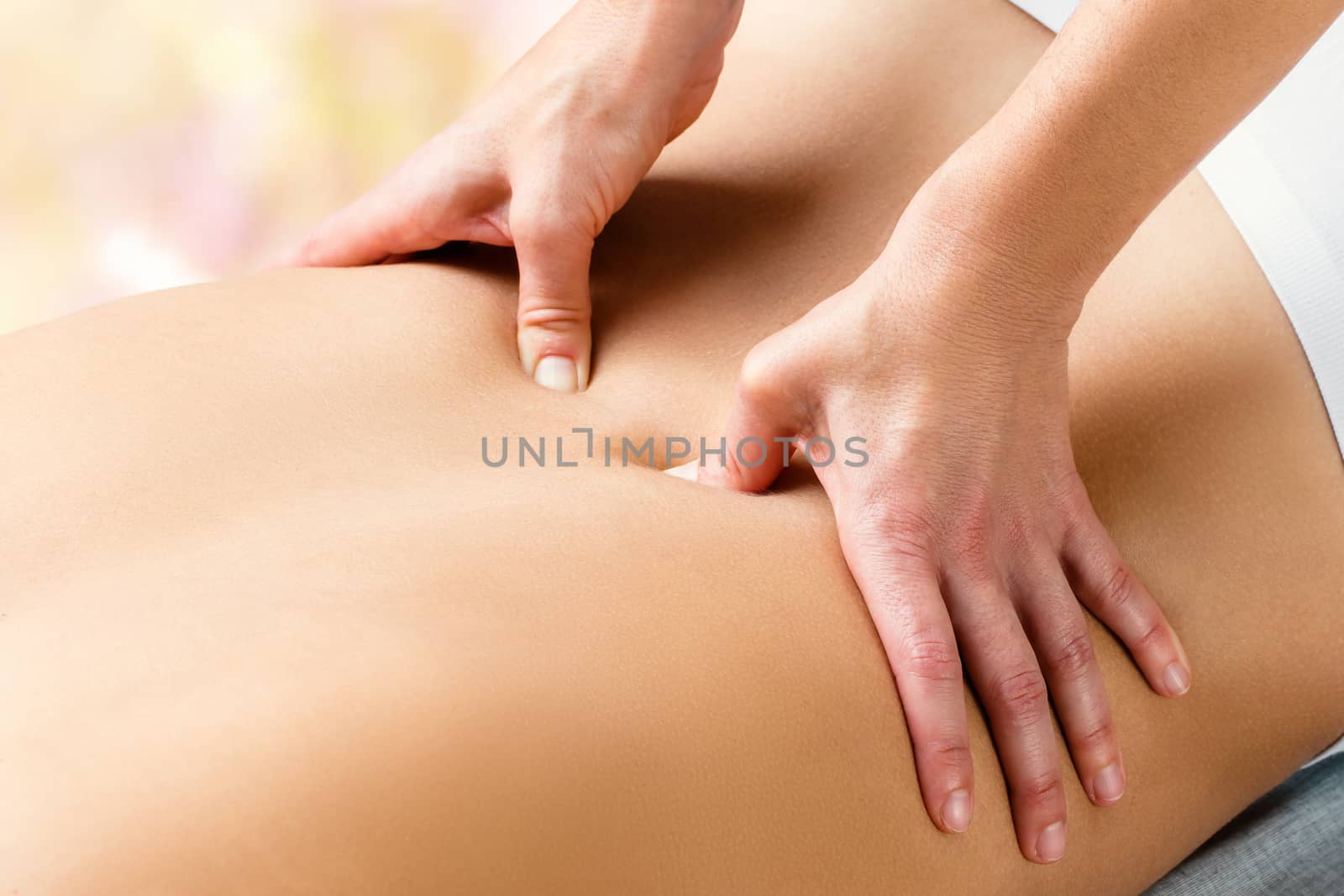 Close up detail of hands applying pressure with thumbs on lower lumbar area on woman.