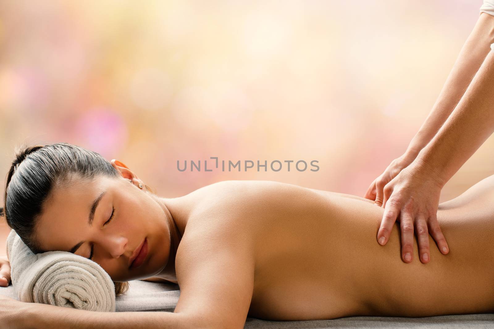 Medium side view portrait of young woman having hot aromatic oil massage is spa.Therapist applying pressure on spinal column.