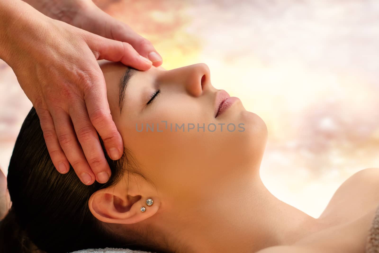 Close up face shot of woman enjoying facial therapy in spa.Therapist massaging fore head with thumbs. 